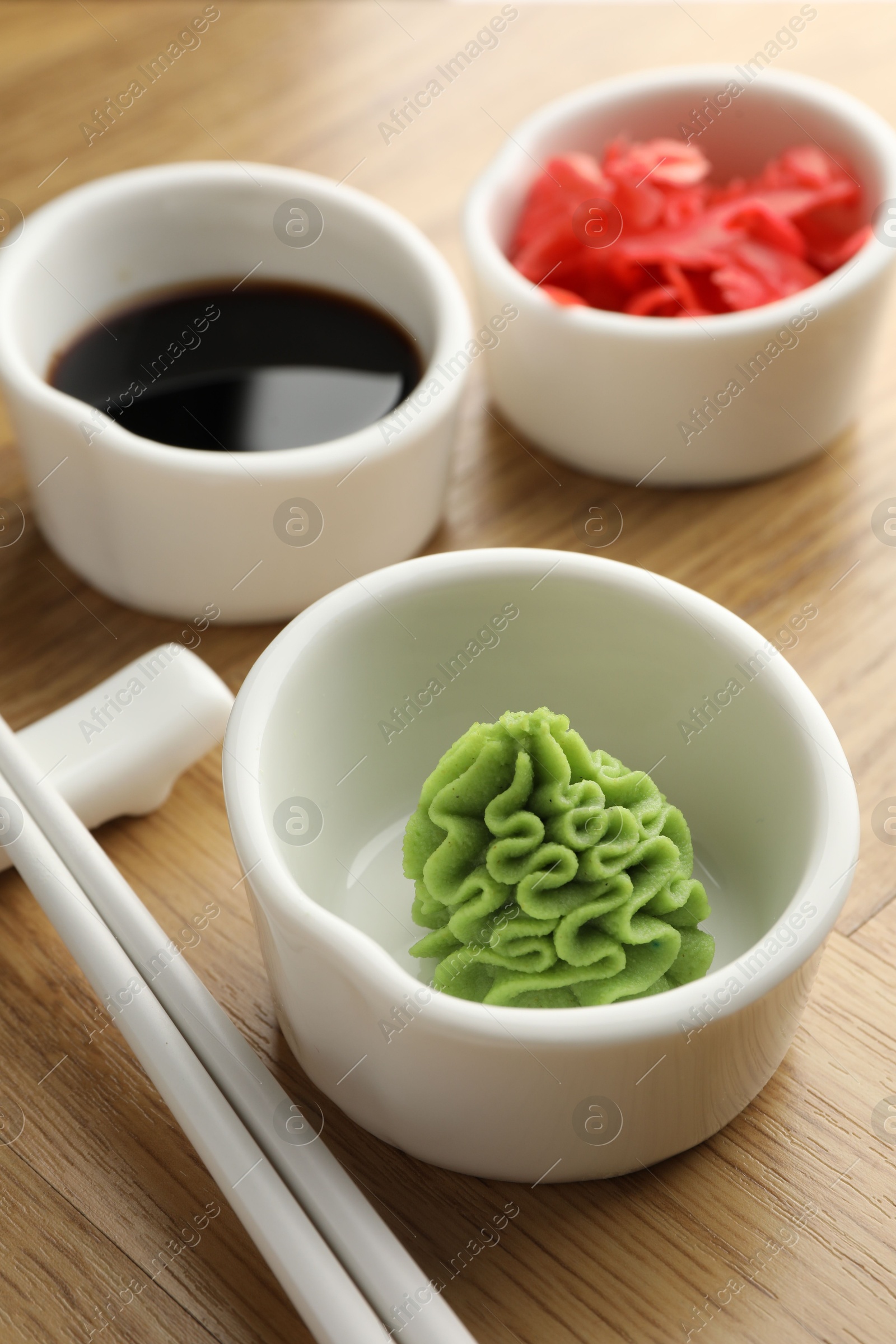 Photo of Hot wasabi paste, soy sauce, ginger and chopsticks on wooden table, closeup