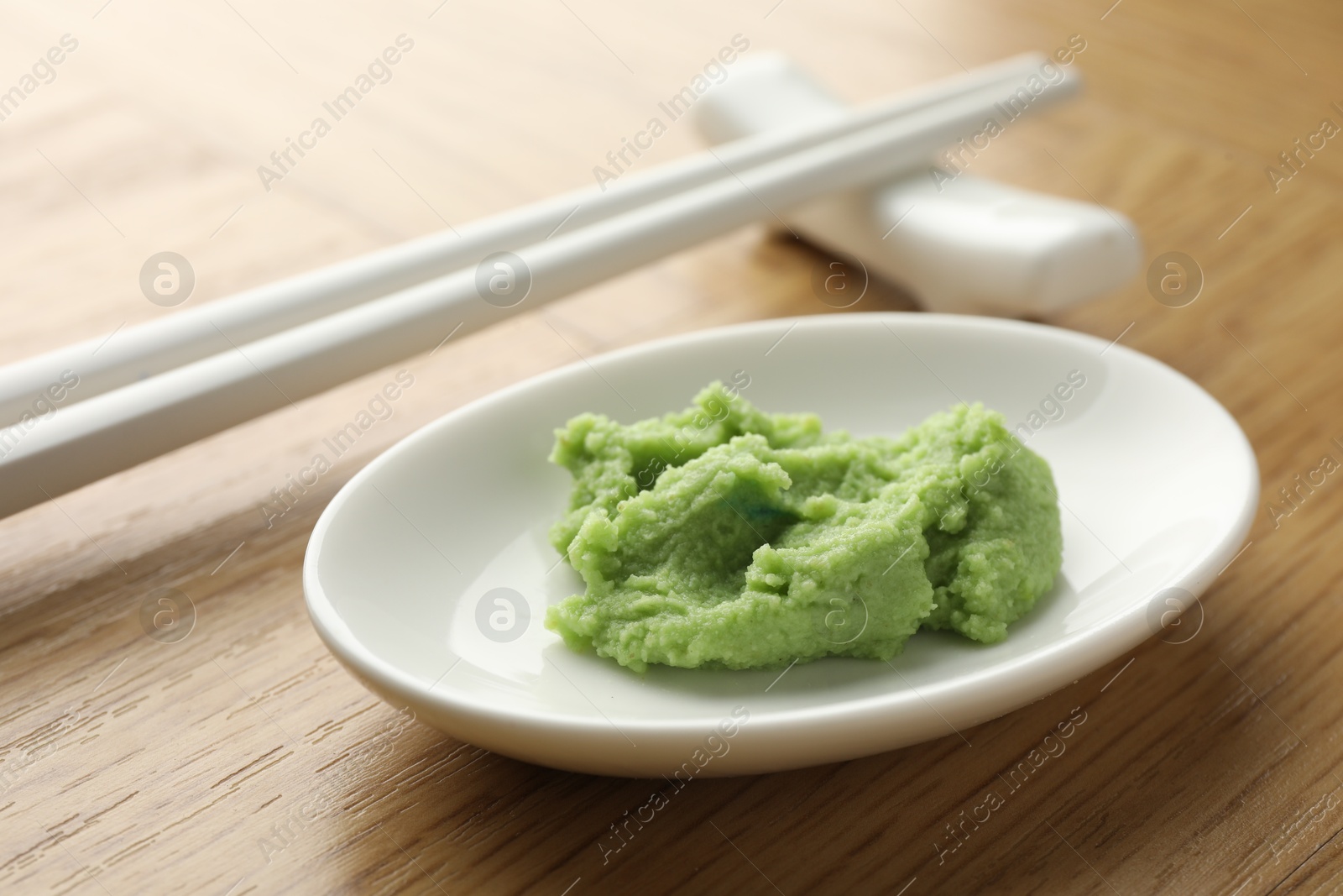 Photo of Hot wasabi paste and chopsticks on wooden table, closeup