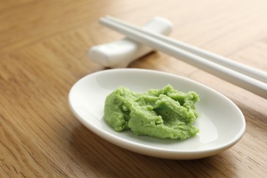 Photo of Hot wasabi paste and chopsticks on wooden table, closeup