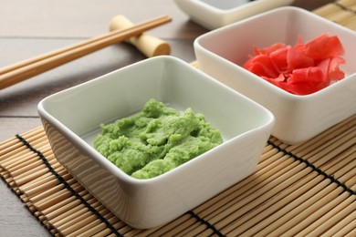 Photo of Hot wasabi paste, ginger and chopsticks on wooden table, closeup