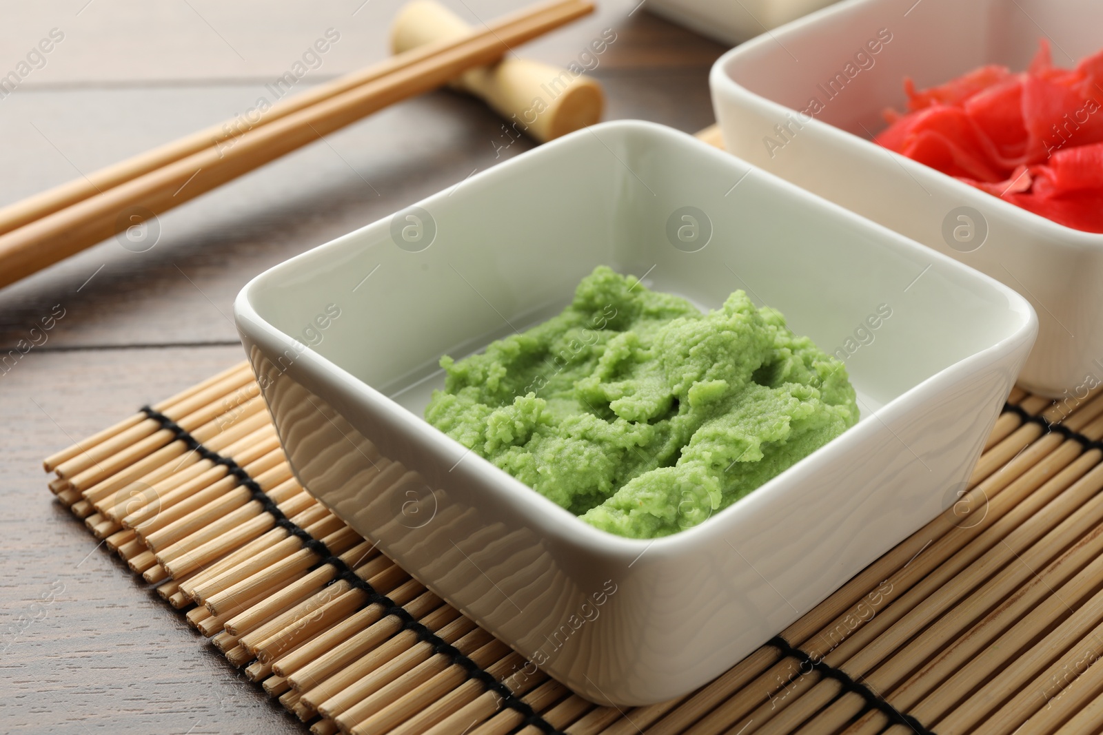 Photo of Hot wasabi paste, ginger and chopsticks on wooden table, closeup