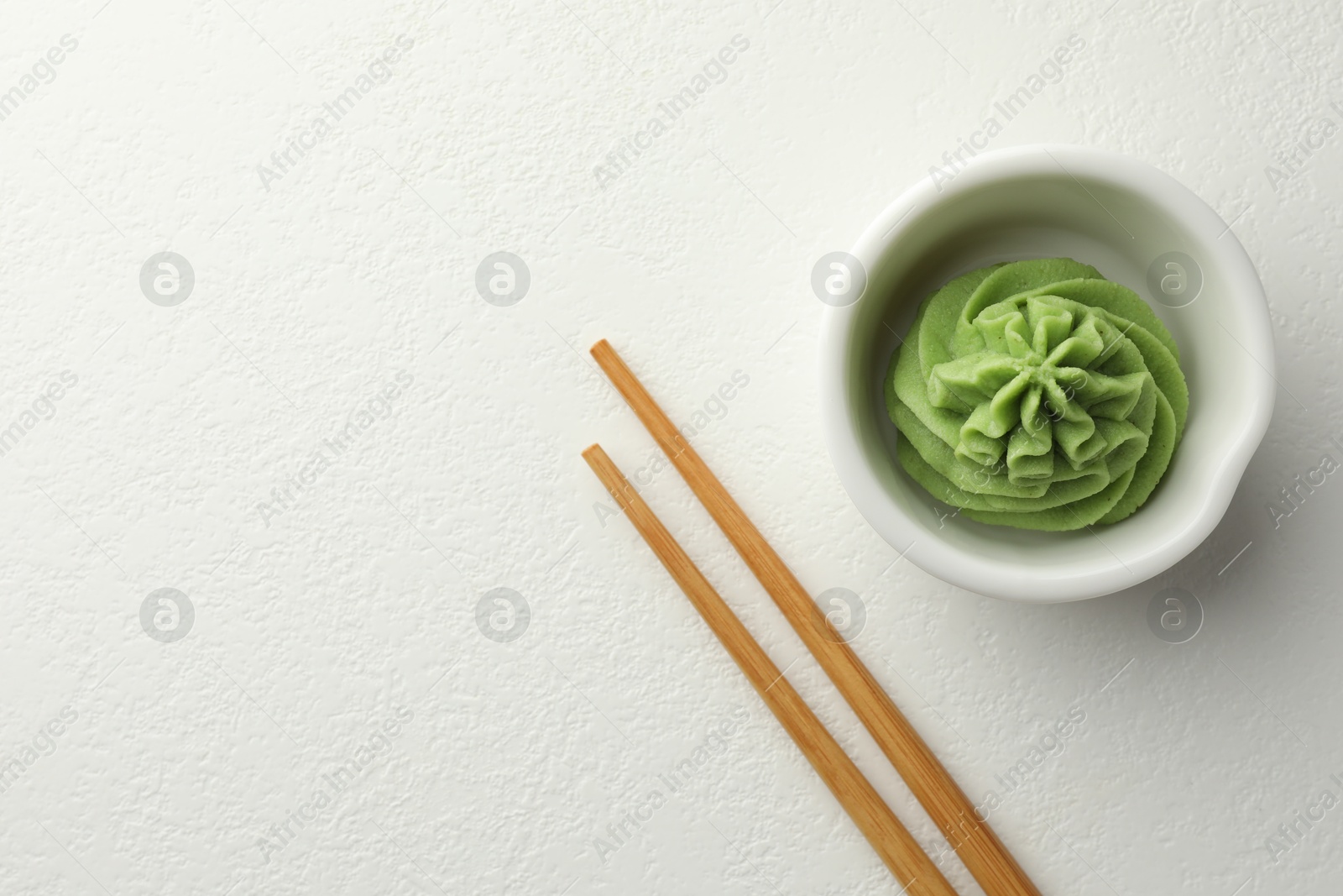 Photo of Hot wasabi paste in bowl and chopsticks on white table, top view. Space for text