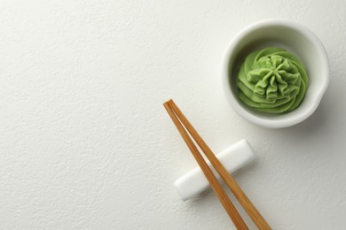 Photo of Hot wasabi paste in bowl and chopsticks on white table, top view. Space for text