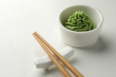 Photo of Hot wasabi paste in bowl and chopsticks on white table, closeup