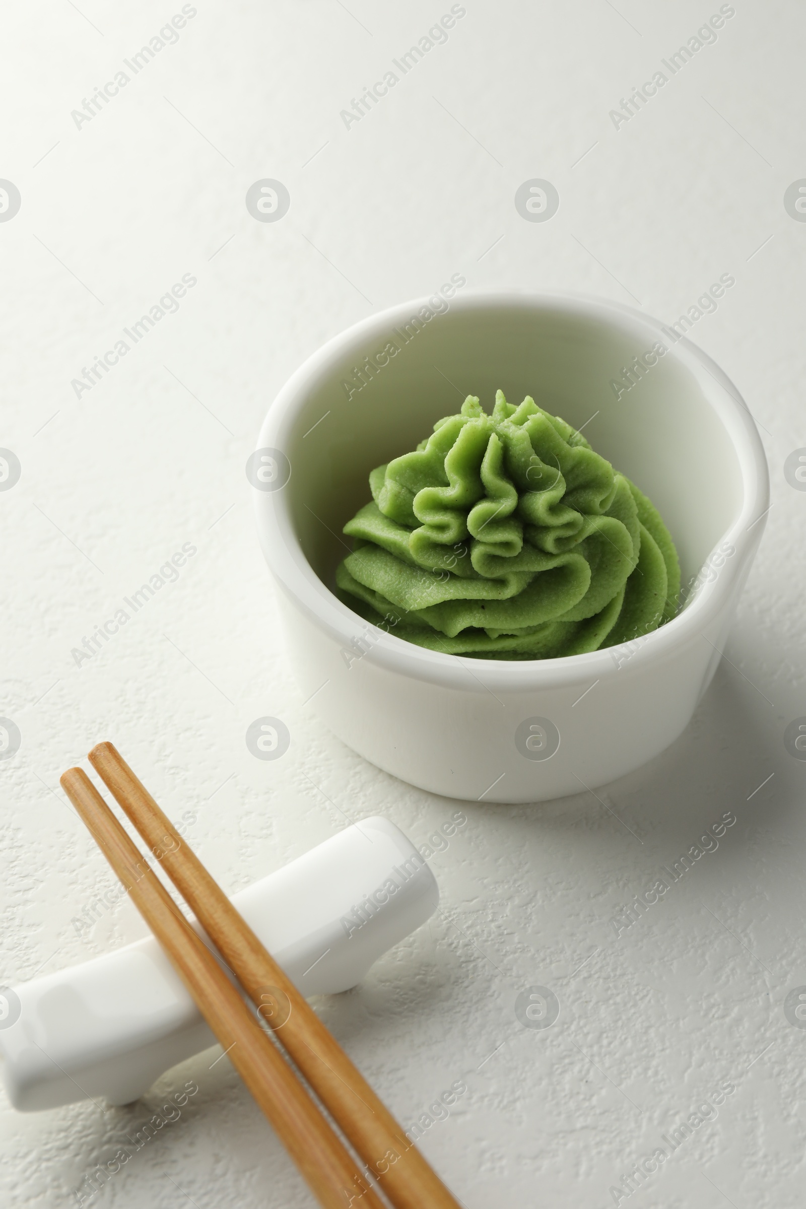 Photo of Hot wasabi paste in bowl and chopsticks on white table, closeup