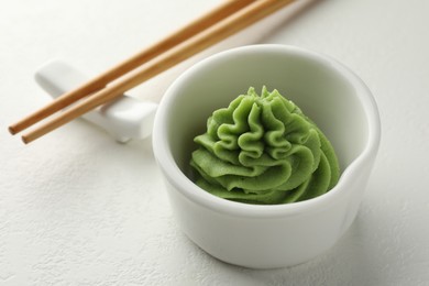 Photo of Hot wasabi paste in bowl and chopsticks on white table, closeup