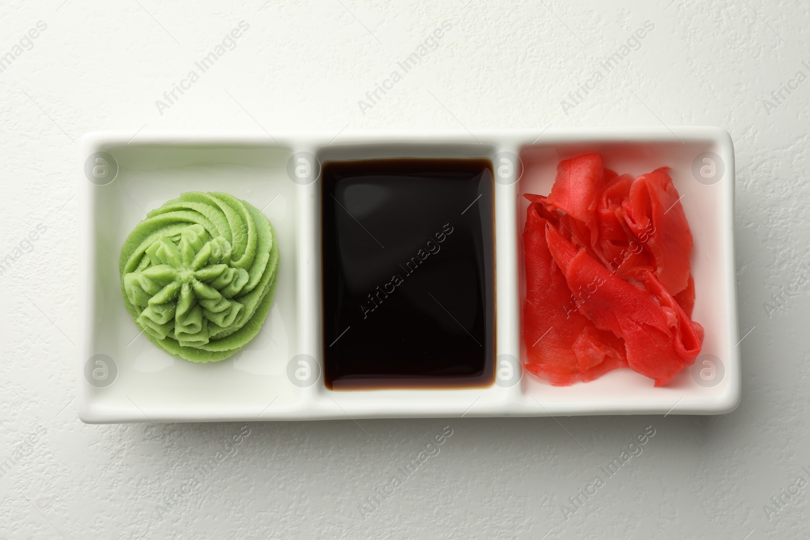 Photo of Hot wasabi paste, soy sauce and ginger on white table, top view