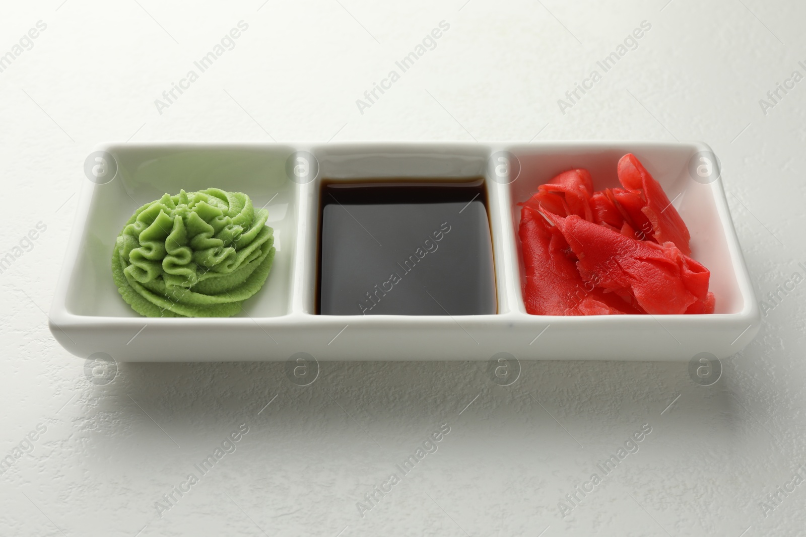 Photo of Hot wasabi paste, soy sauce and ginger on white table, closeup