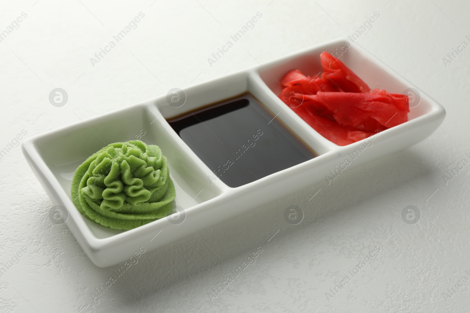 Photo of Hot wasabi paste, soy sauce and ginger on white table, closeup