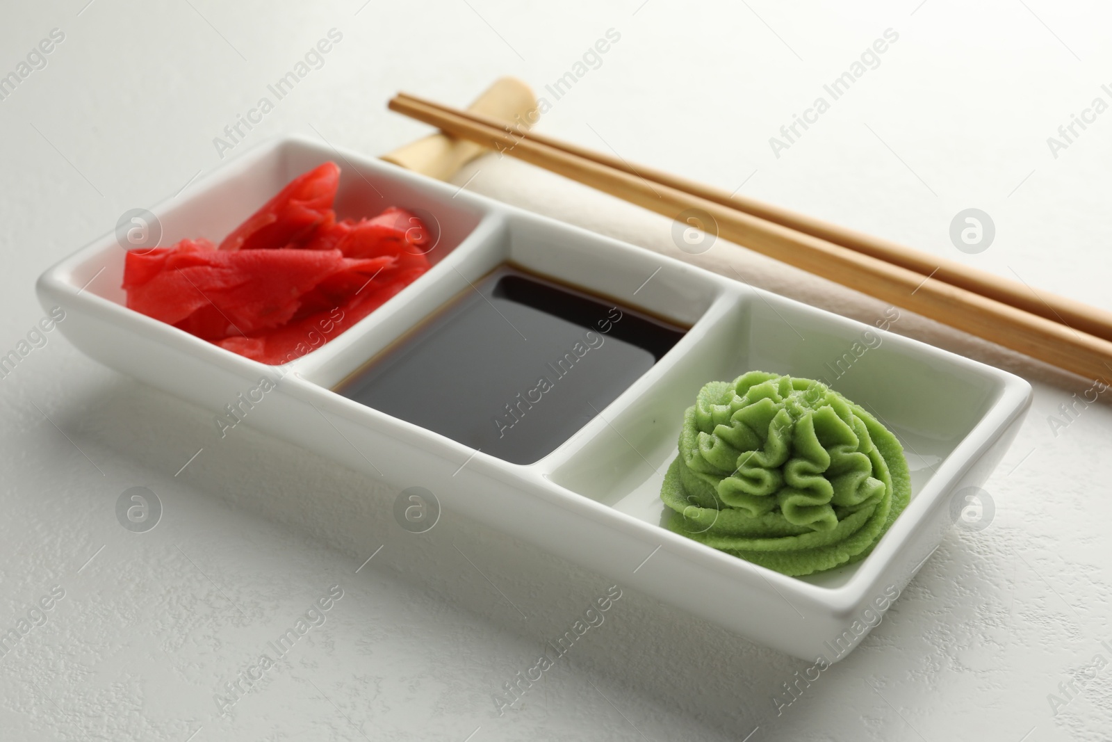 Photo of Hot wasabi paste, soy sauce, ginger and chopsticks on white table, closeup