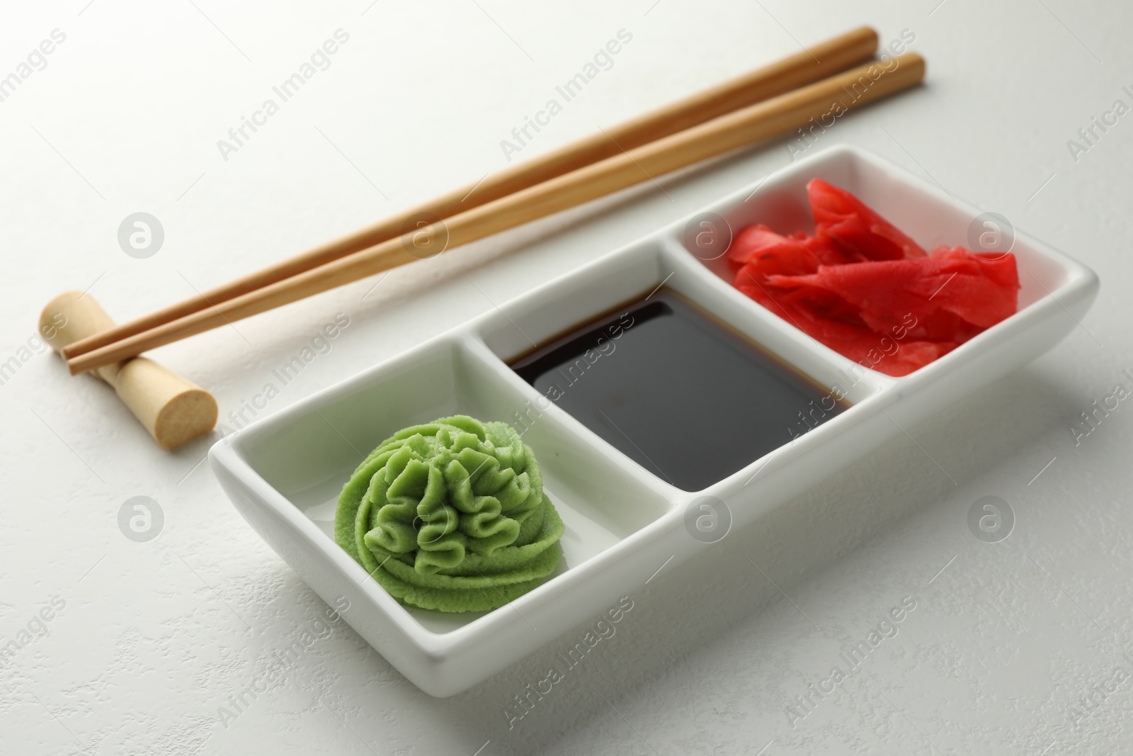 Photo of Hot wasabi paste, soy sauce, ginger and chopsticks on white table, closeup