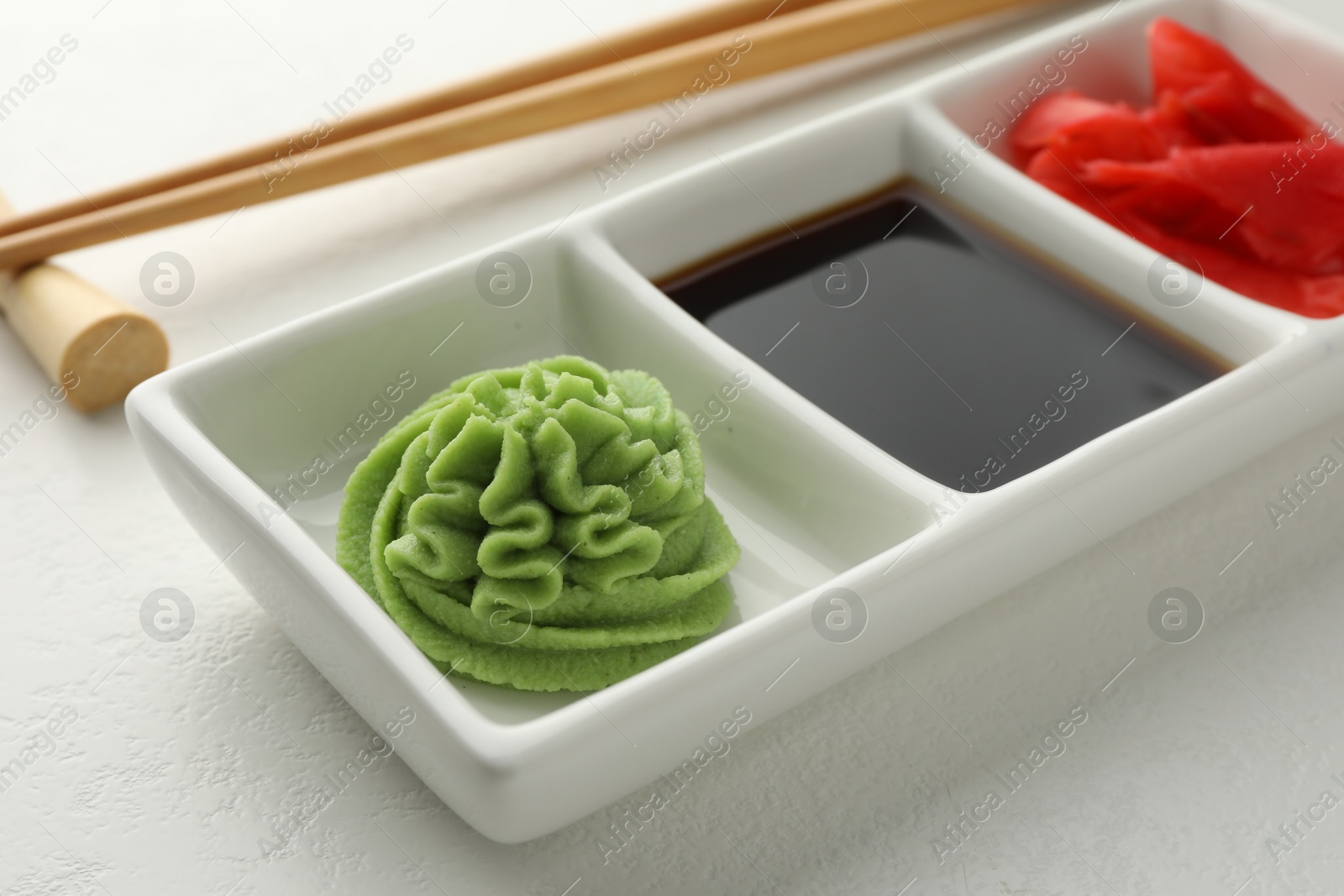 Photo of Hot wasabi paste, soy sauce, ginger and chopsticks on white table, closeup