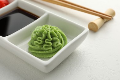 Photo of Hot wasabi paste, soy sauce and chopsticks on white table, closeup