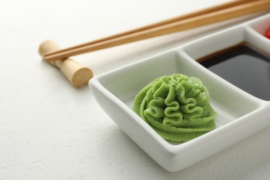 Photo of Hot wasabi paste, soy sauce and chopsticks on white table, closeup