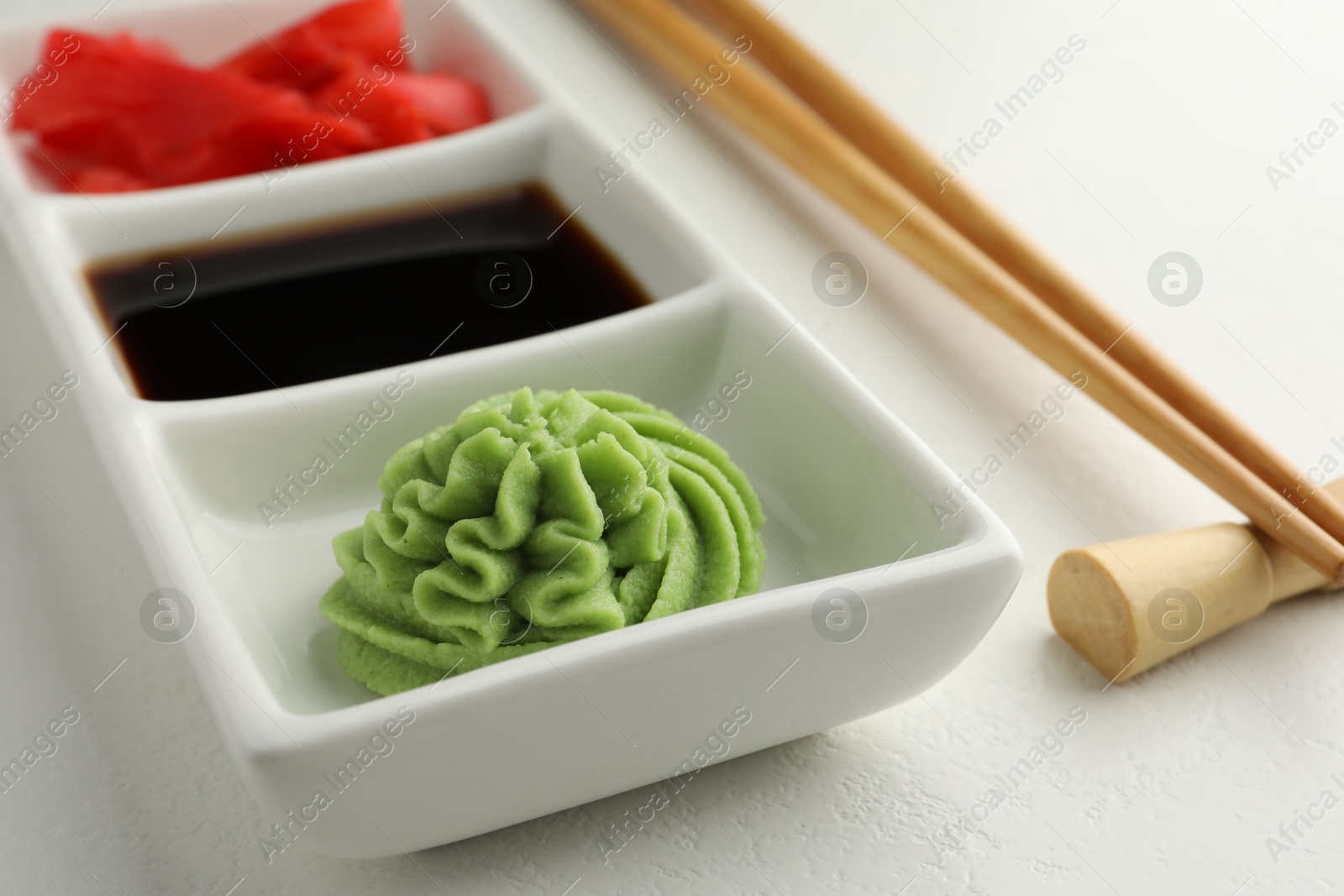 Photo of Hot wasabi paste, soy sauce, ginger and chopsticks on white table, closeup