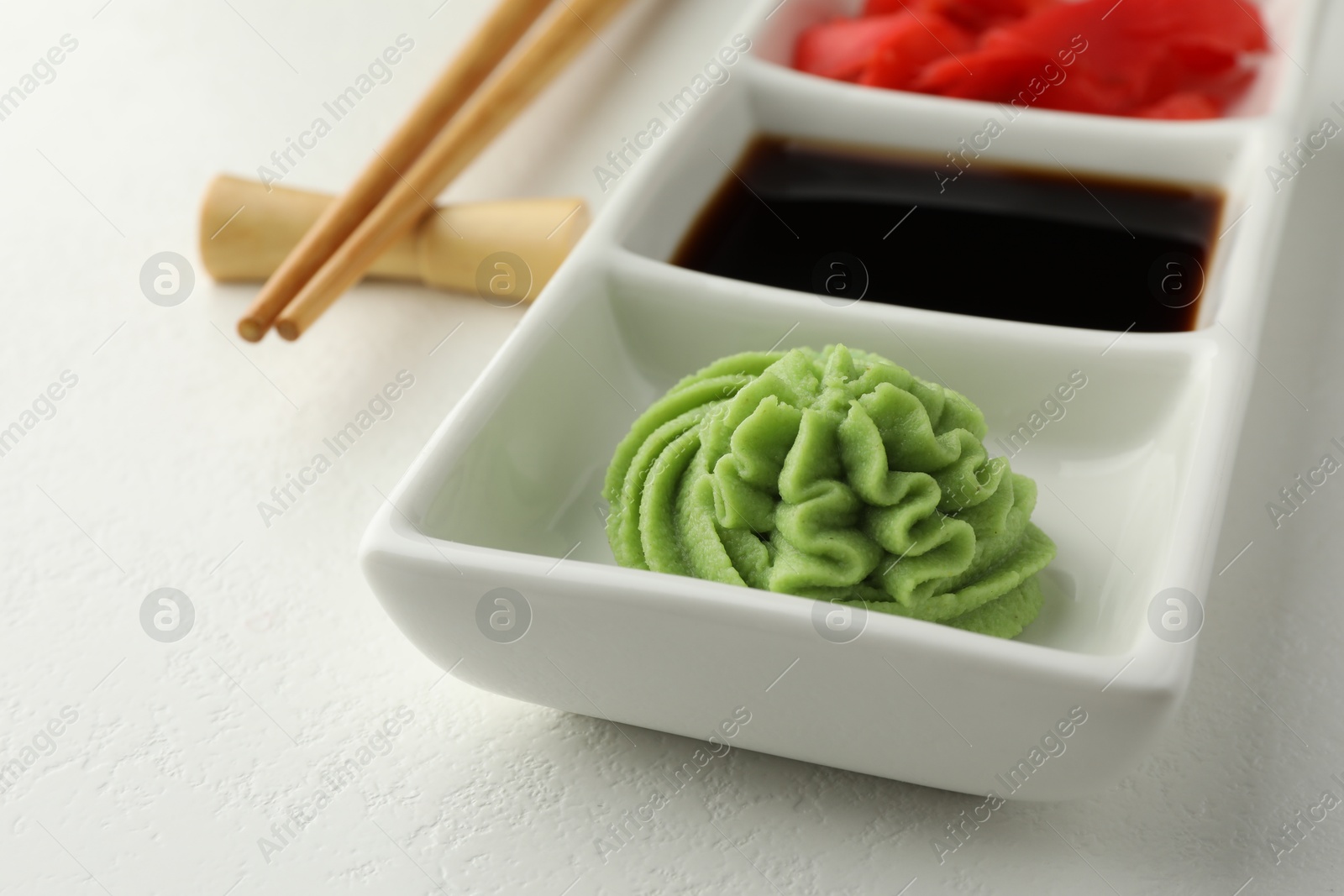 Photo of Hot wasabi paste, soy sauce, ginger and chopsticks on white table, closeup