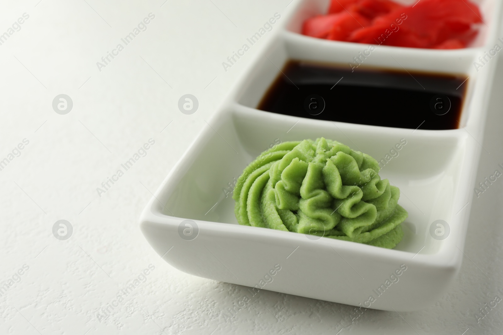 Photo of Hot wasabi paste, soy sauce and ginger on white table, closeup. Space for text