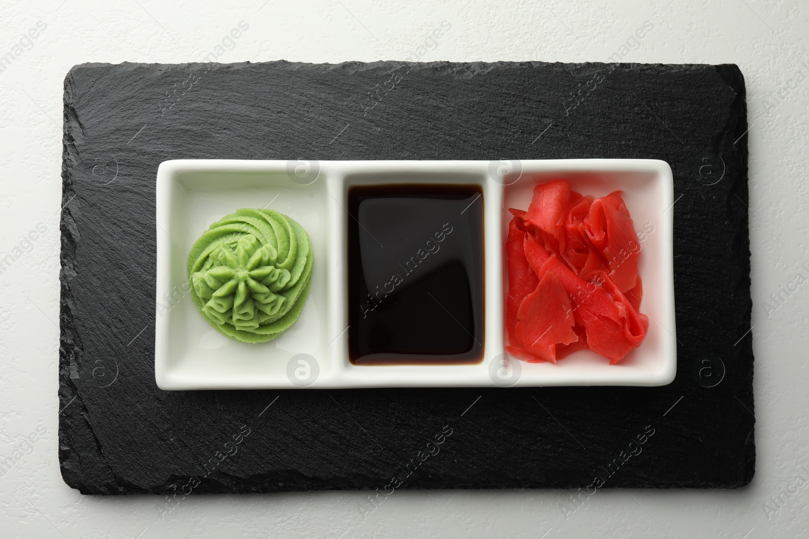 Photo of Hot wasabi paste, soy sauce and ginger on white table, top view