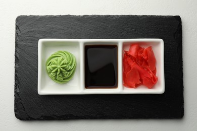 Photo of Hot wasabi paste, soy sauce and ginger on white table, top view