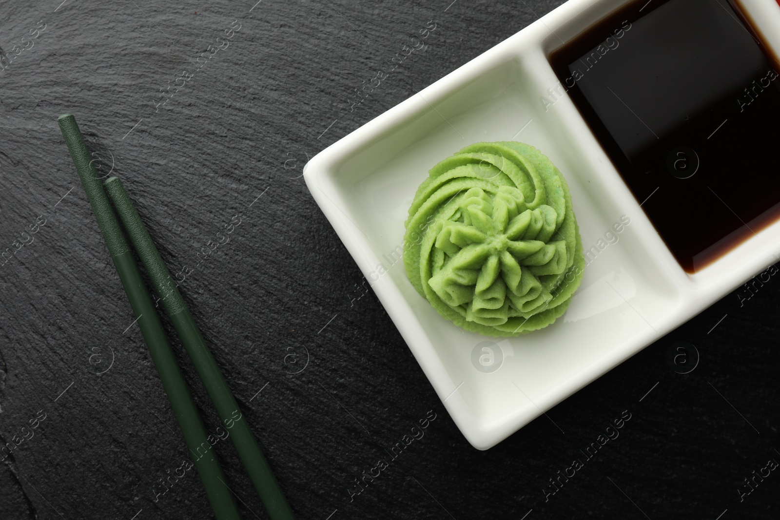 Photo of Hot wasabi paste, soy sauce and chopsticks on grey table, top view