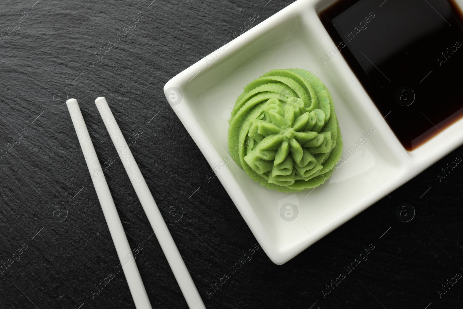 Photo of Hot wasabi paste, soy sauce and chopsticks on grey table, top view