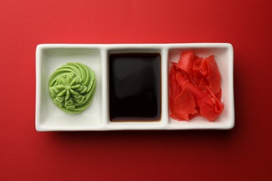 Photo of Hot wasabi paste, soy sauce and ginger on red table, top view