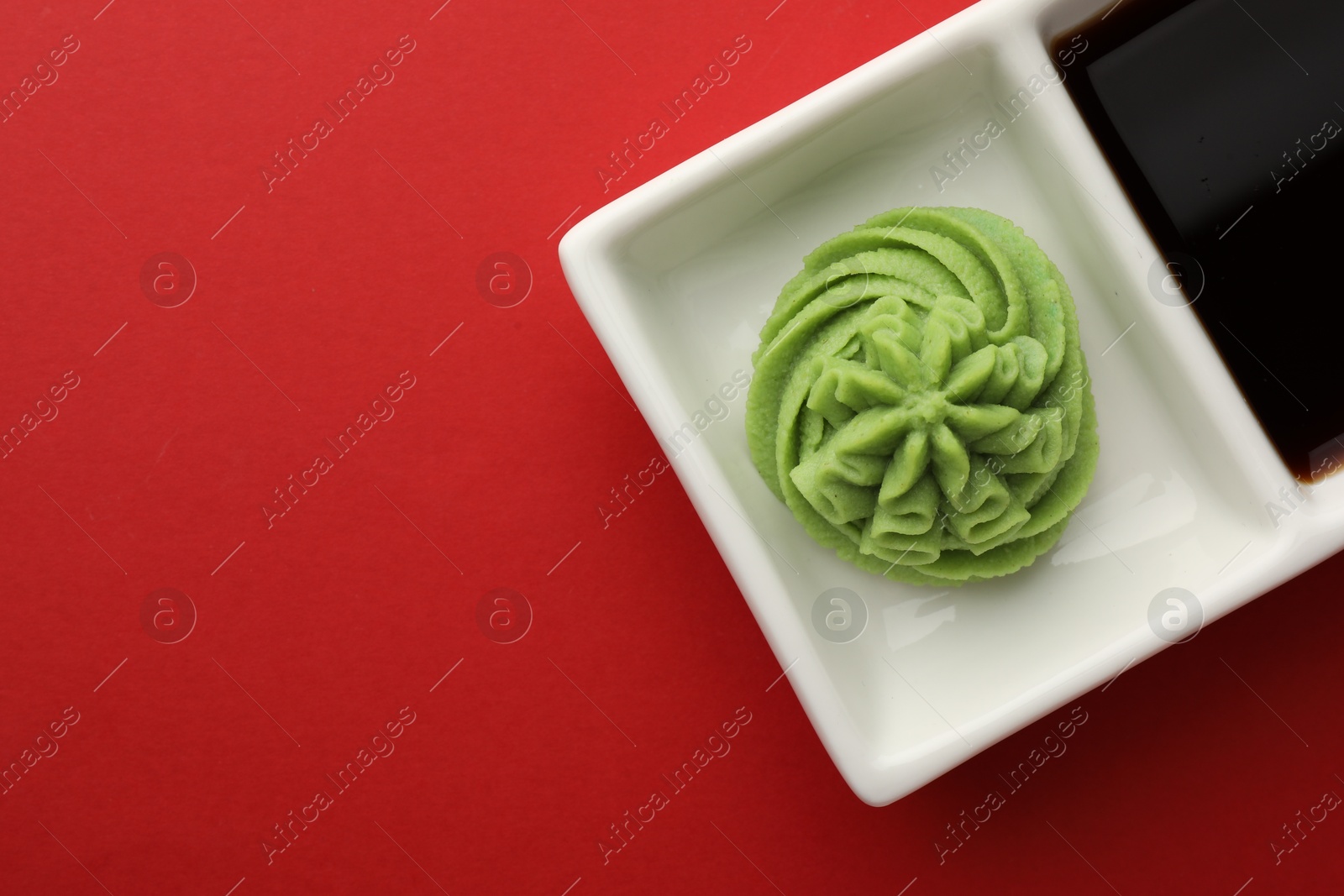 Photo of Hot wasabi paste and soy sauce on red table, top view. Space for text