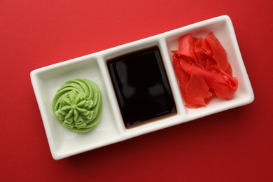 Photo of Hot wasabi paste, soy sauce and ginger on red table, top view