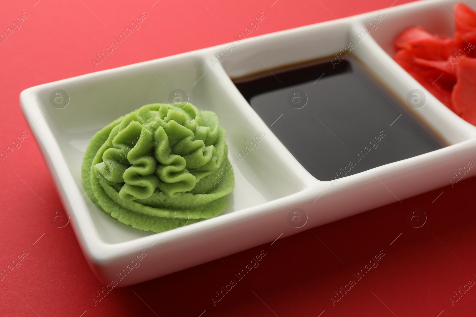 Photo of Hot wasabi paste, soy sauce and ginger on red table, closeup