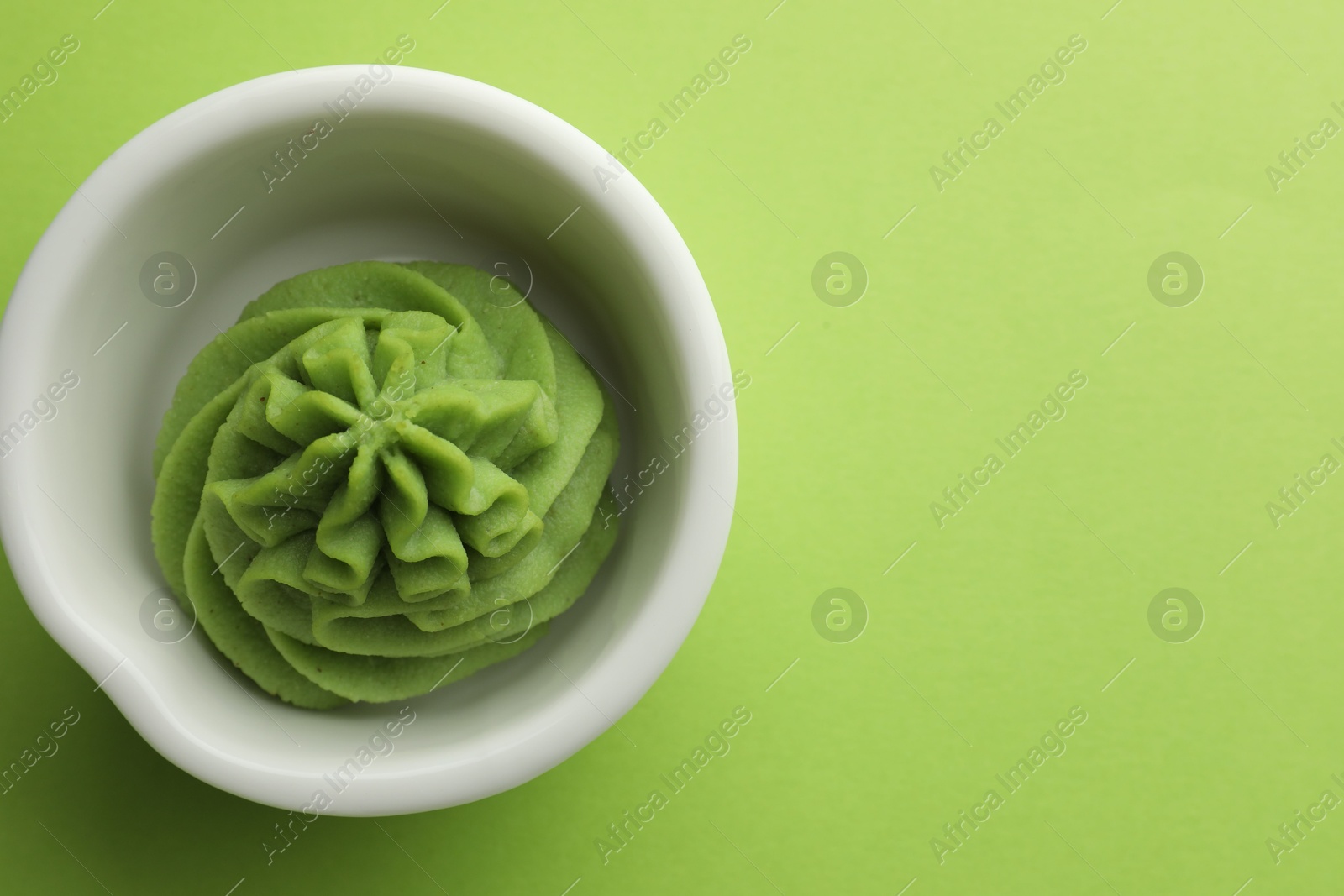 Photo of Hot wasabi paste in bowl on green table, top view. Space for text