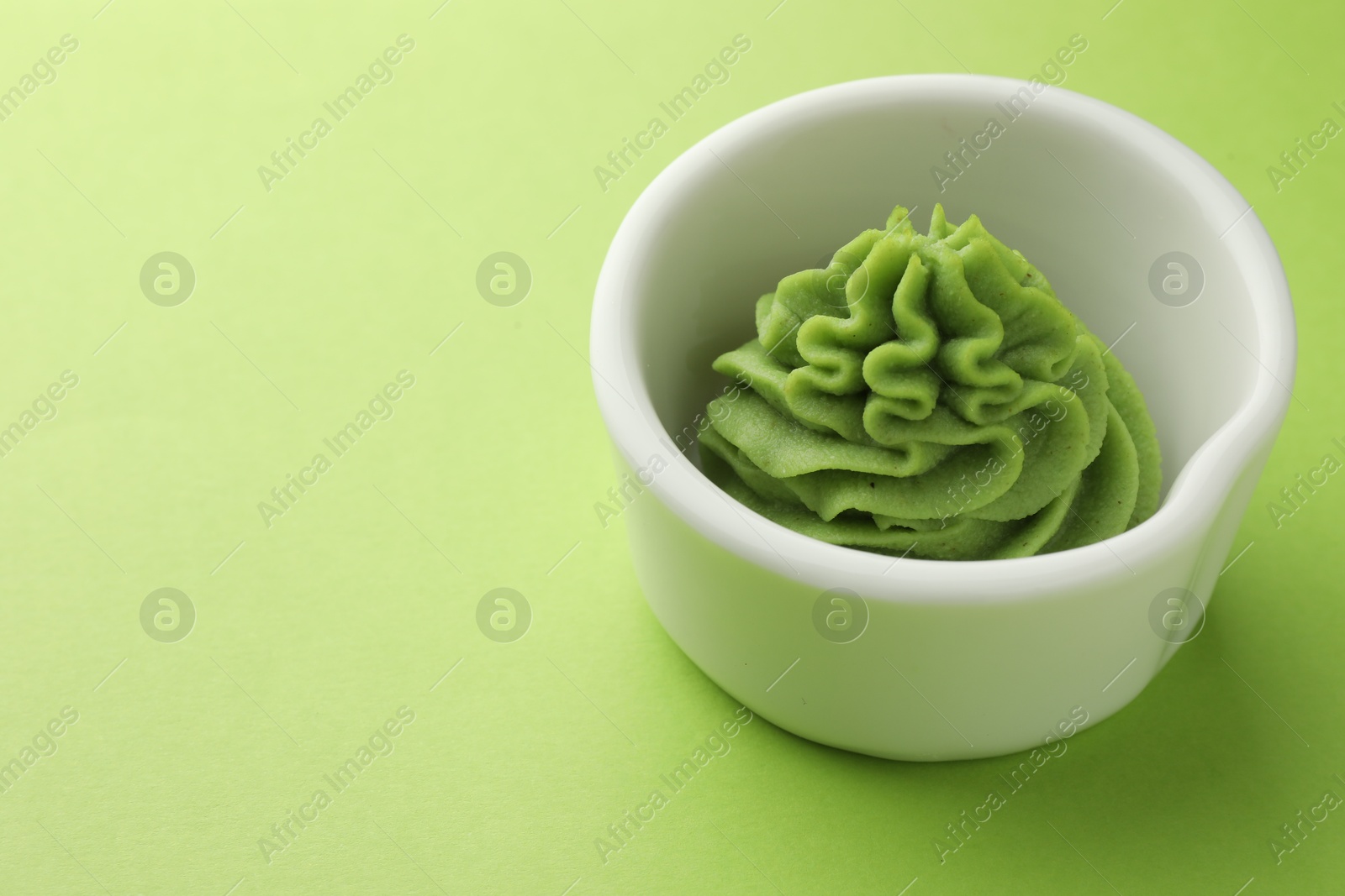 Photo of Hot wasabi paste in bowl on green table, closeup. Space for text