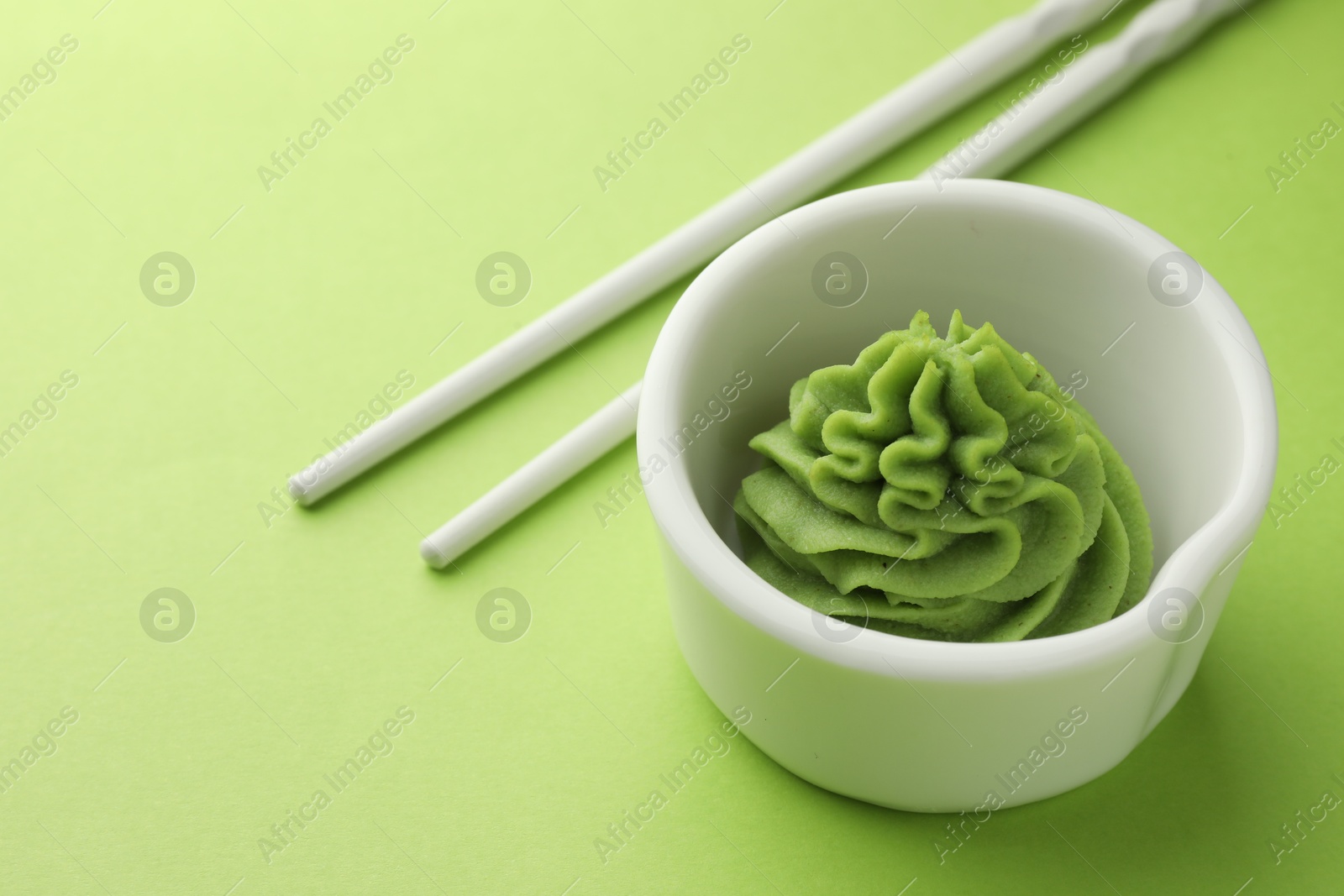 Photo of Hot wasabi paste in bowl and chopsticks on green table, closeup. Space for text