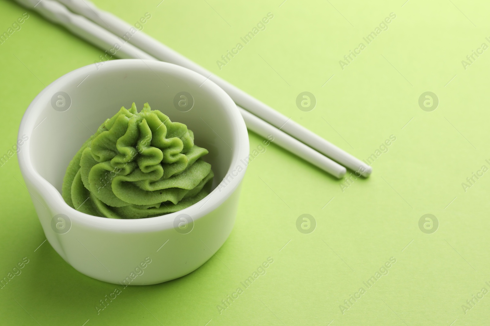 Photo of Hot wasabi paste in bowl and chopsticks on green table, closeup. Space for text