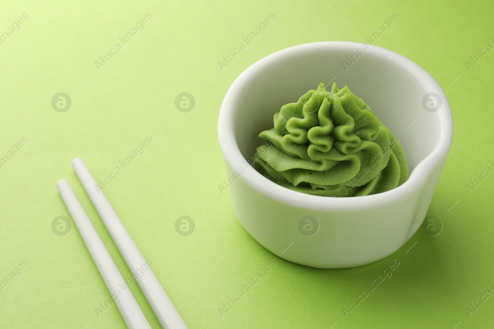 Photo of Hot wasabi paste in bowl and chopsticks on green table, closeup. Space for text