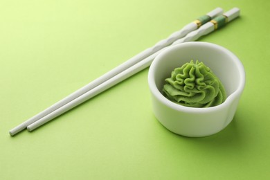 Photo of Hot wasabi paste in bowl and chopsticks on green table, closeup