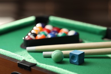 Photo of Many colorful billiard balls in triangle rack, cues and chalk on green table indoors, closeup