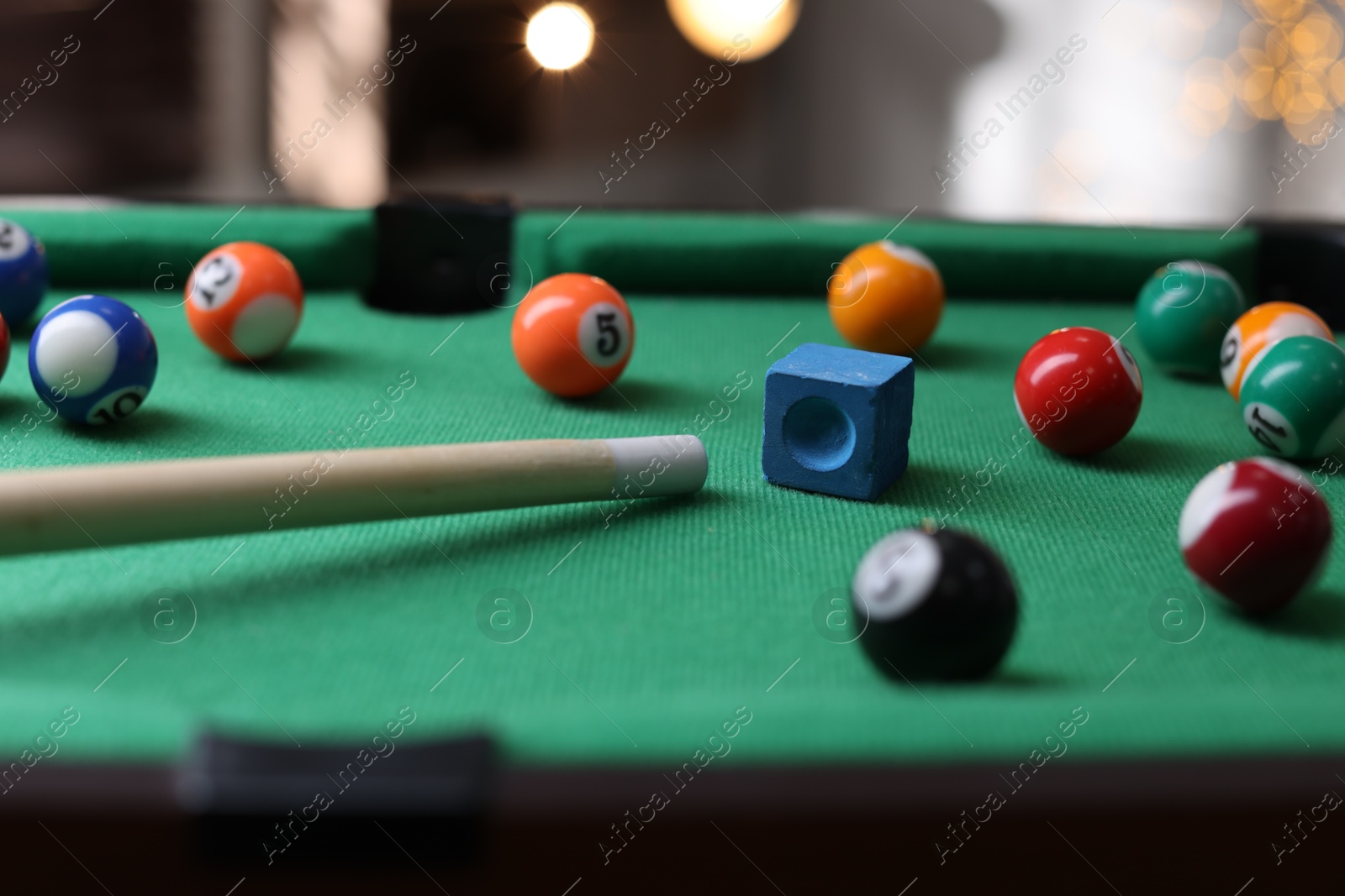 Photo of Many colorful billiard balls, cue and chalk on green table indoors, closeup