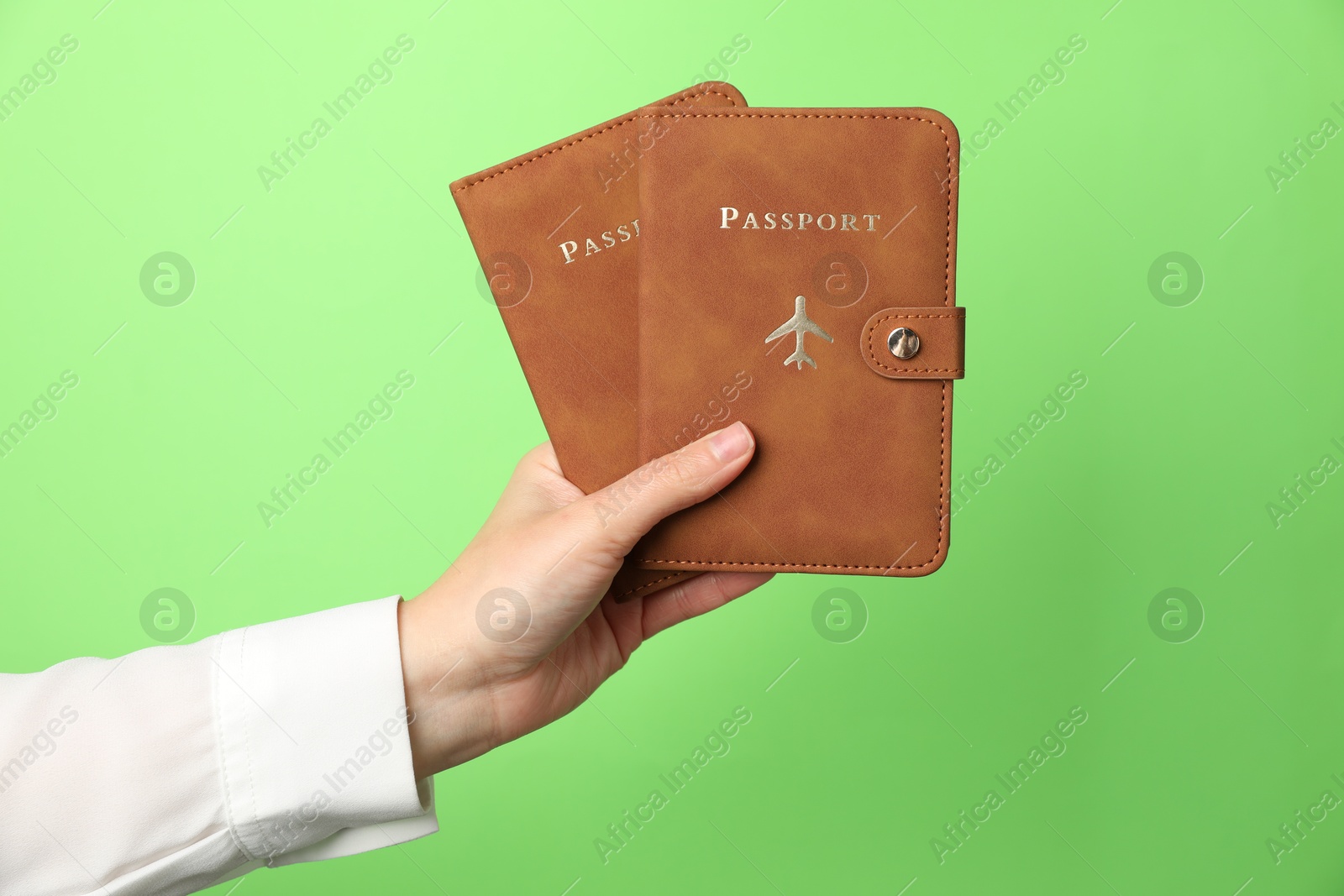 Photo of Woman holding passports in bright covers on green background, closeup