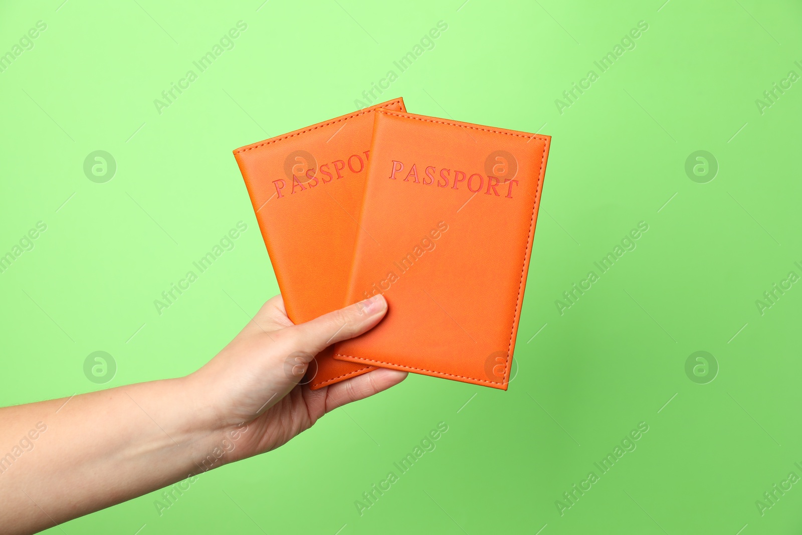 Photo of Woman holding passports in bright covers on green background, closeup