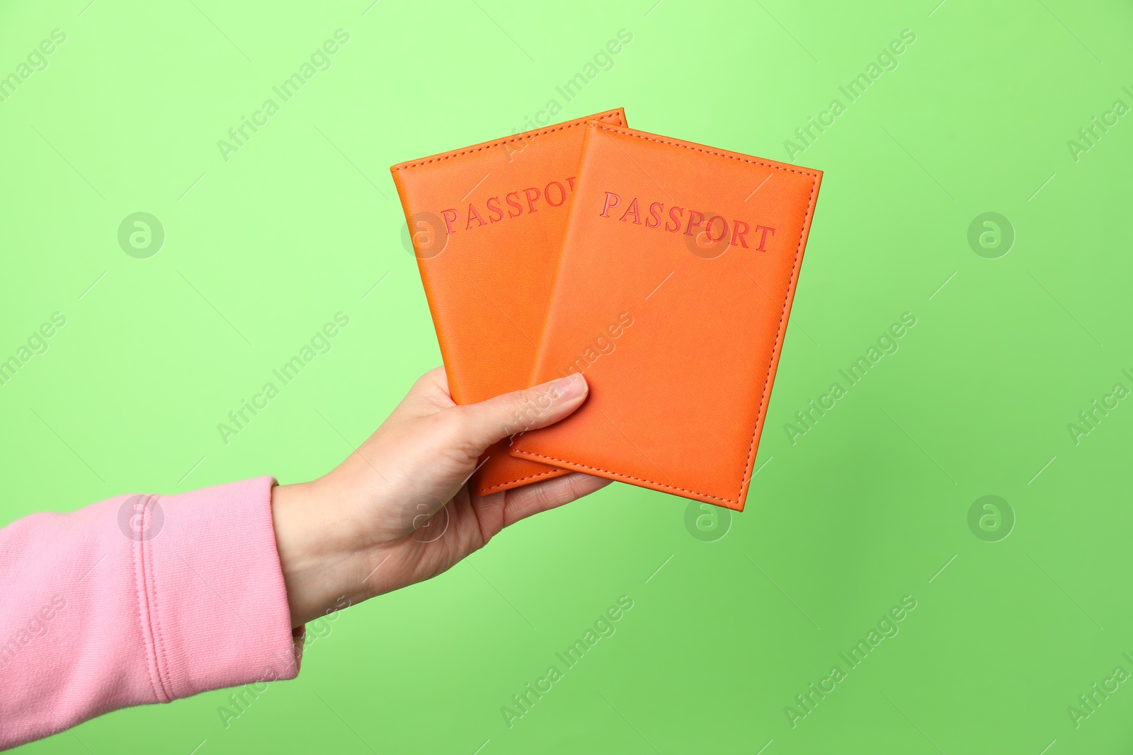 Photo of Woman holding passports in bright covers on green background, closeup