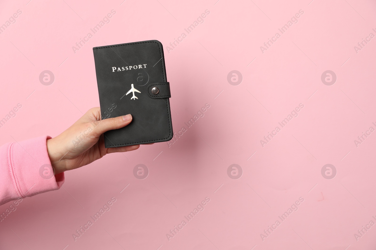 Photo of Woman holding passport in bright cover on pink background, closeup. Space for text