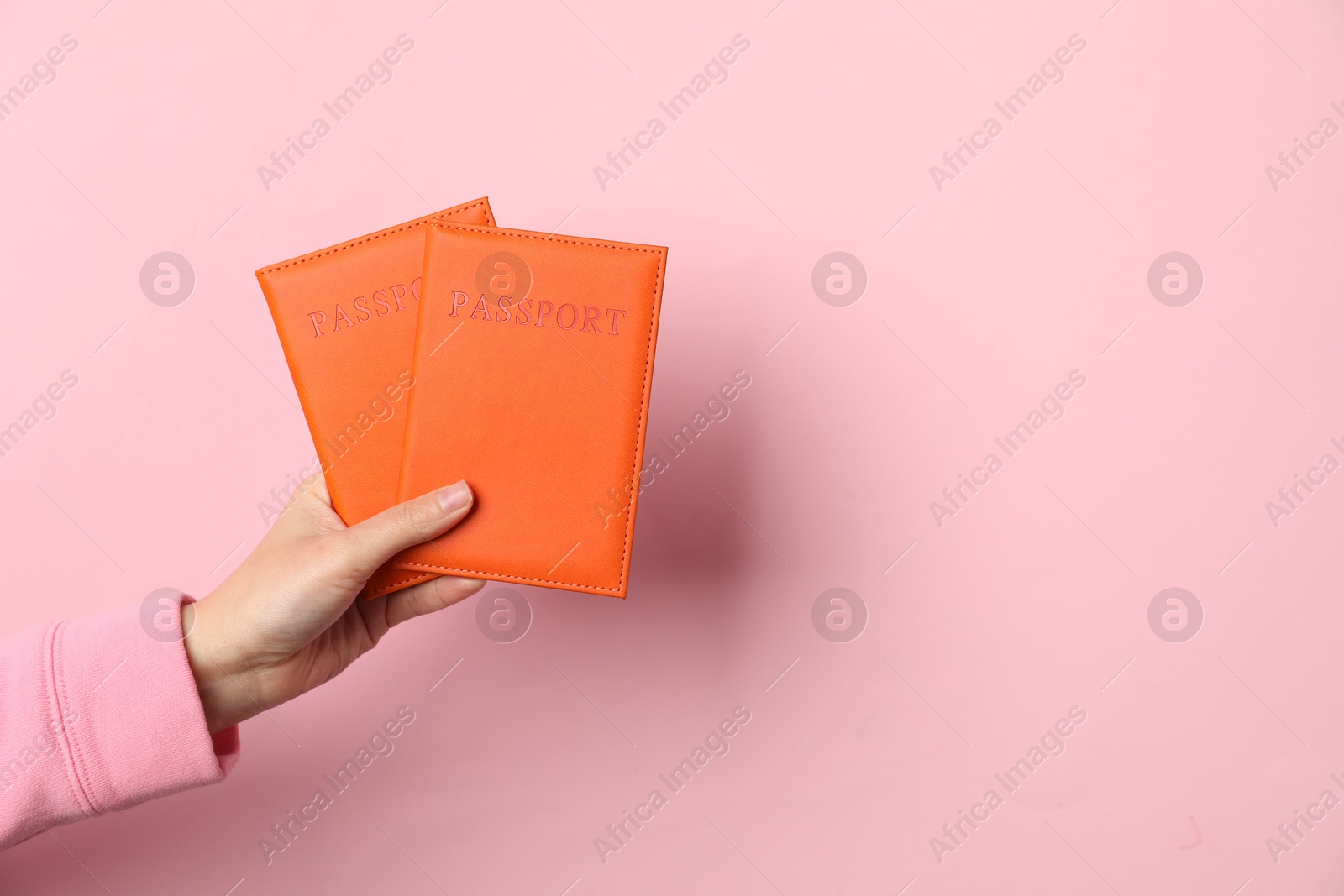 Photo of Woman holding passports in bright covers on pink background, closeup. Space for text