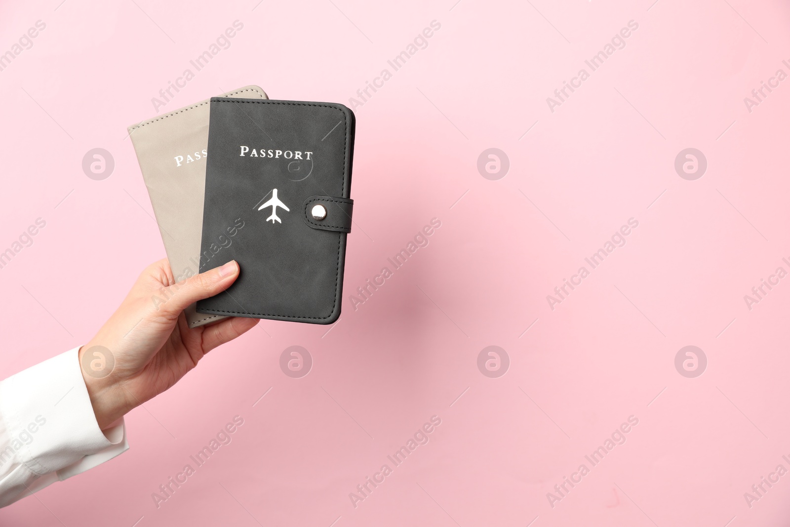 Photo of Woman holding passports in bright covers on pink background, closeup. Space for text