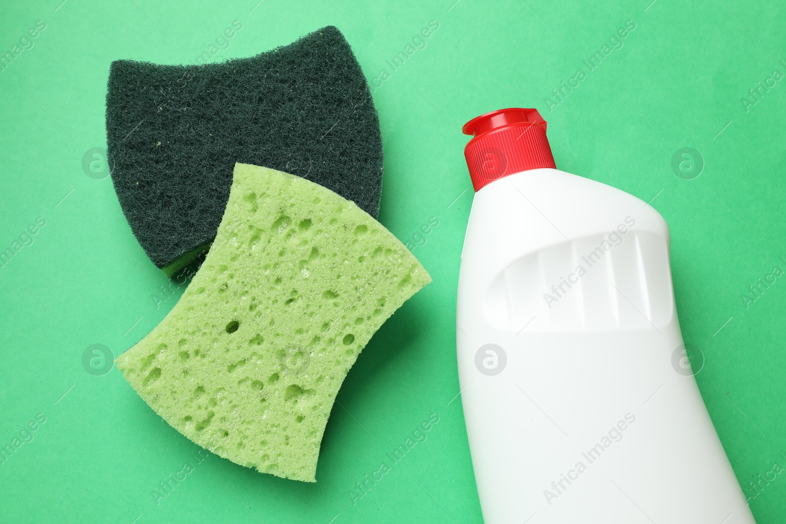 Photo of Sponges and dish soap on green background, top view