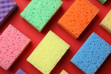 Photo of Colorful sponges on red background, flat lay. Cleaning tool