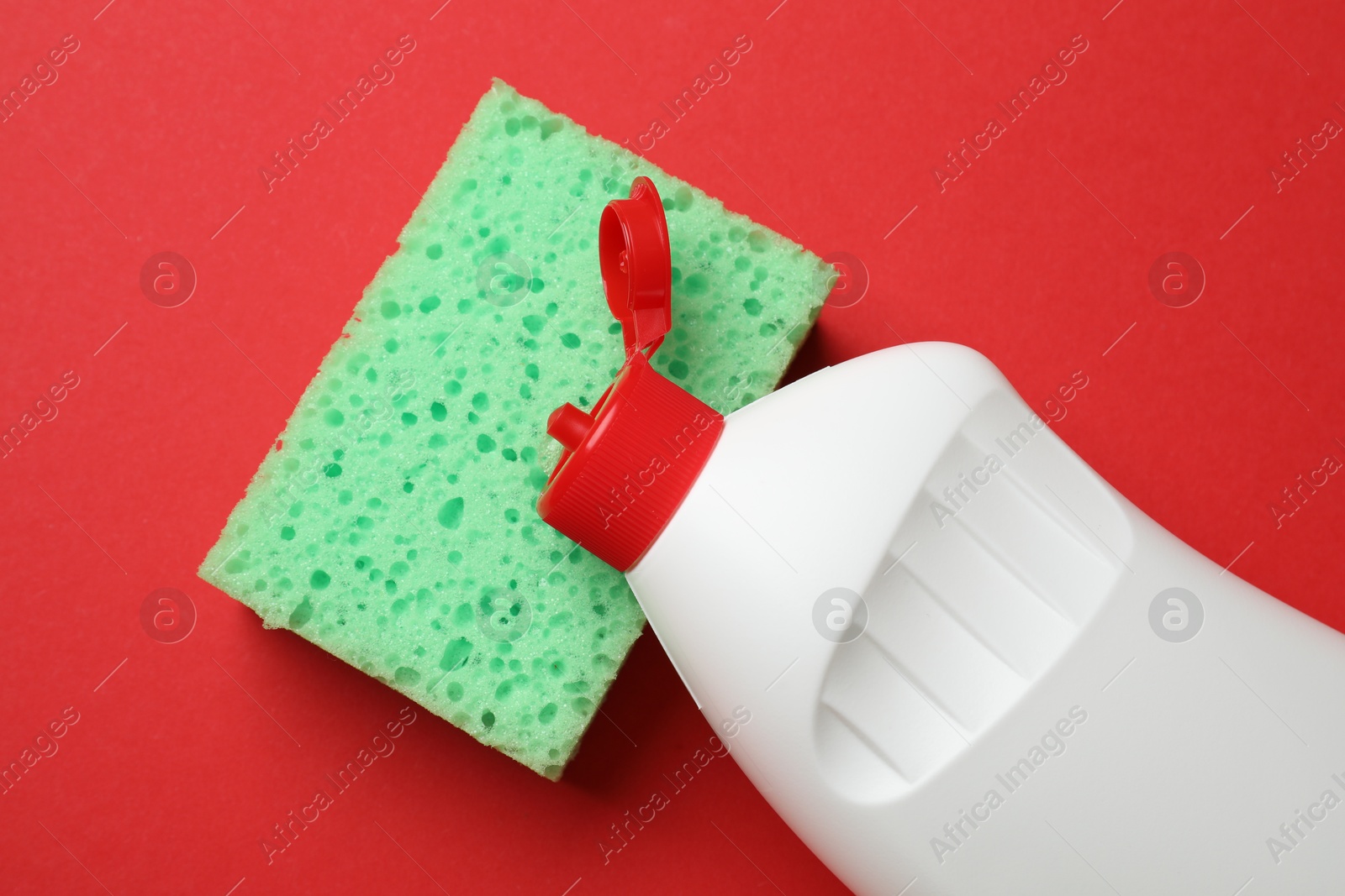 Photo of Sponge and dish soap on red background, top view