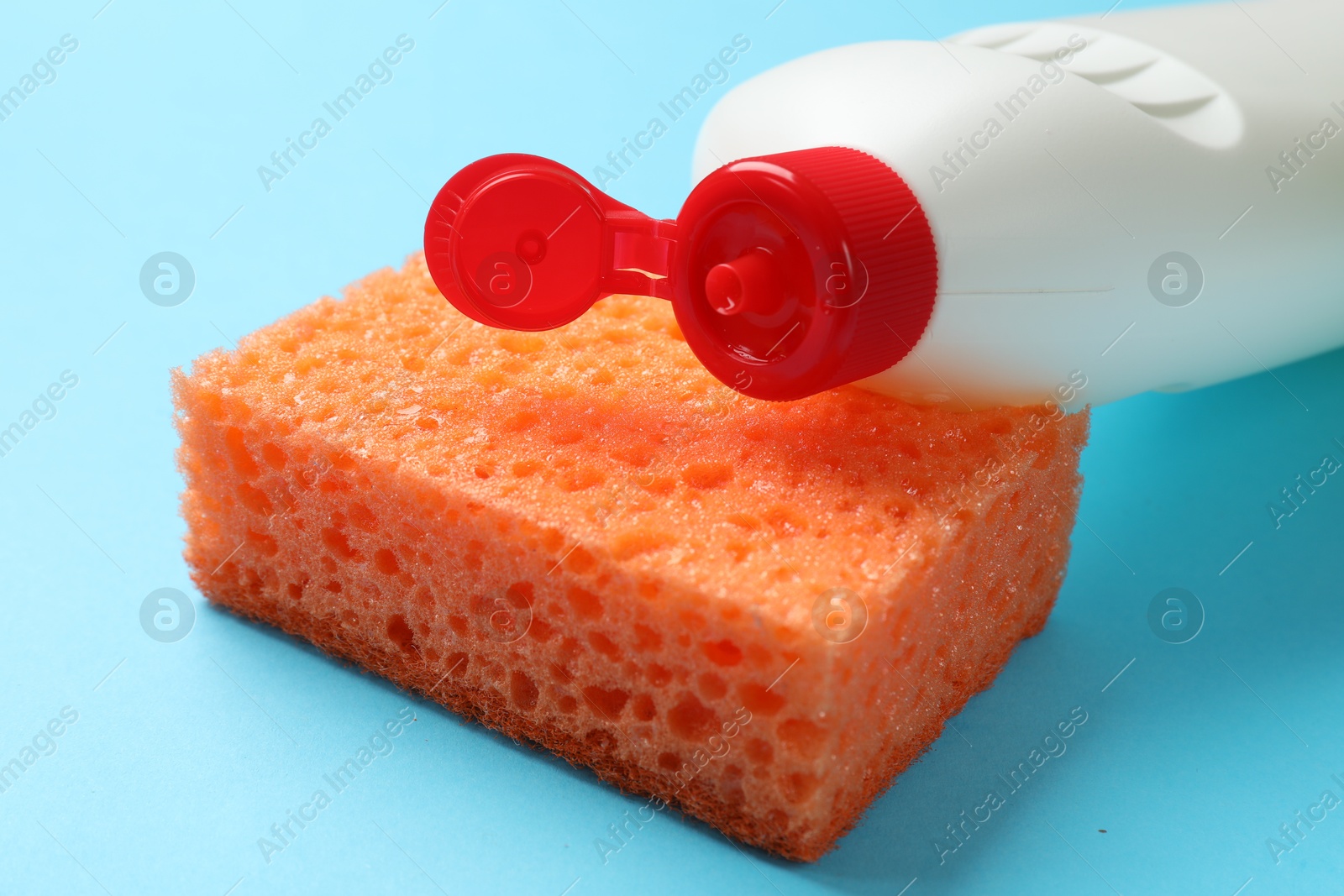 Photo of Sponge and dish soap on light blue background, closeup. Cleaning tool