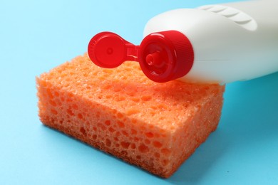 Photo of Sponge and dish soap on light blue background, closeup. Cleaning tool