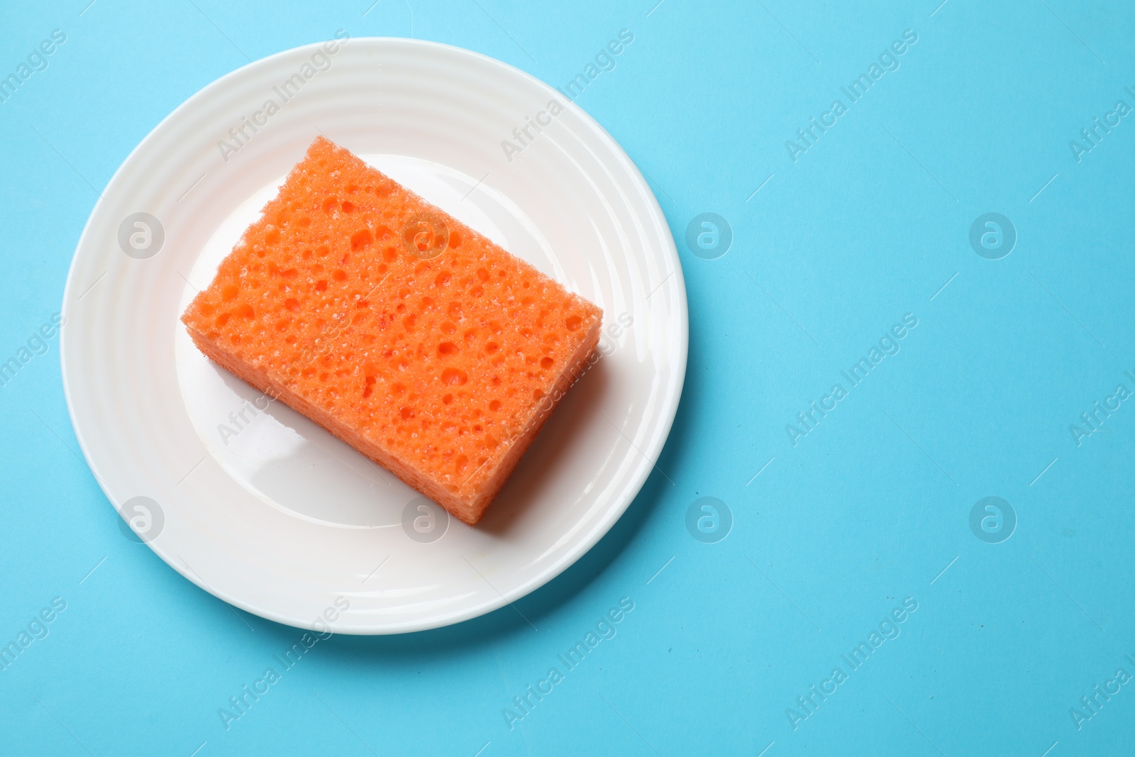 Photo of Plate with sponge on light blue background, top view. Space for text