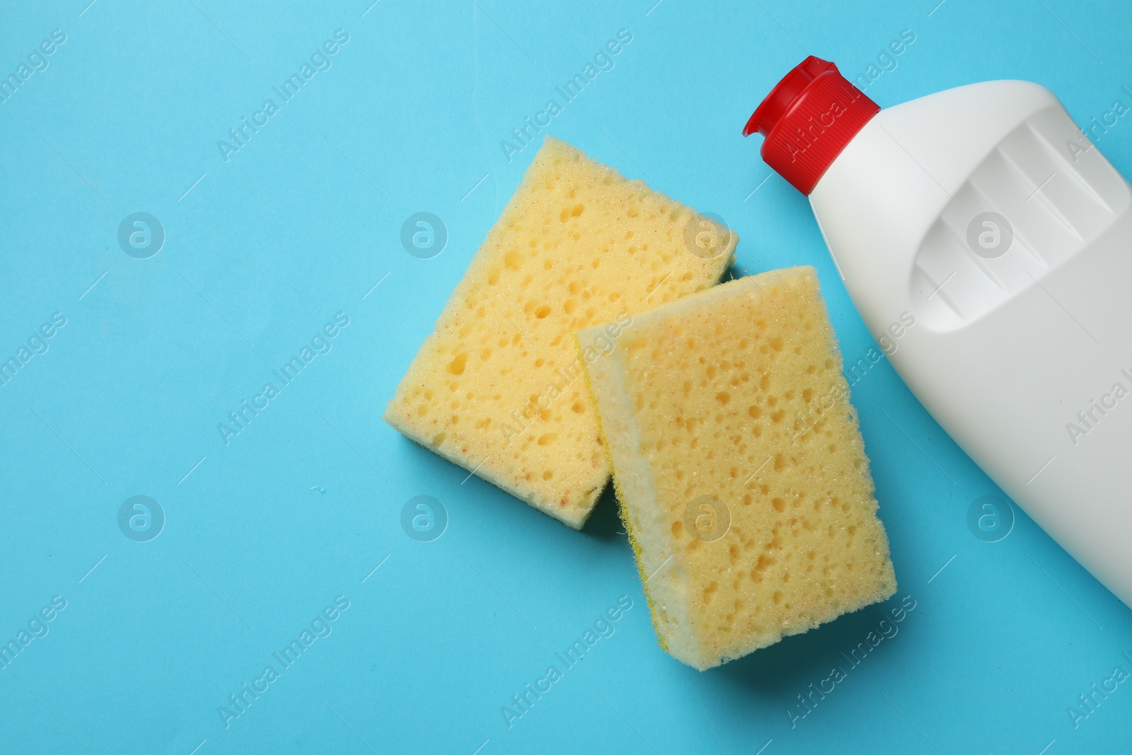 Photo of Sponges and dish soap on light blue background, top view. Space for text